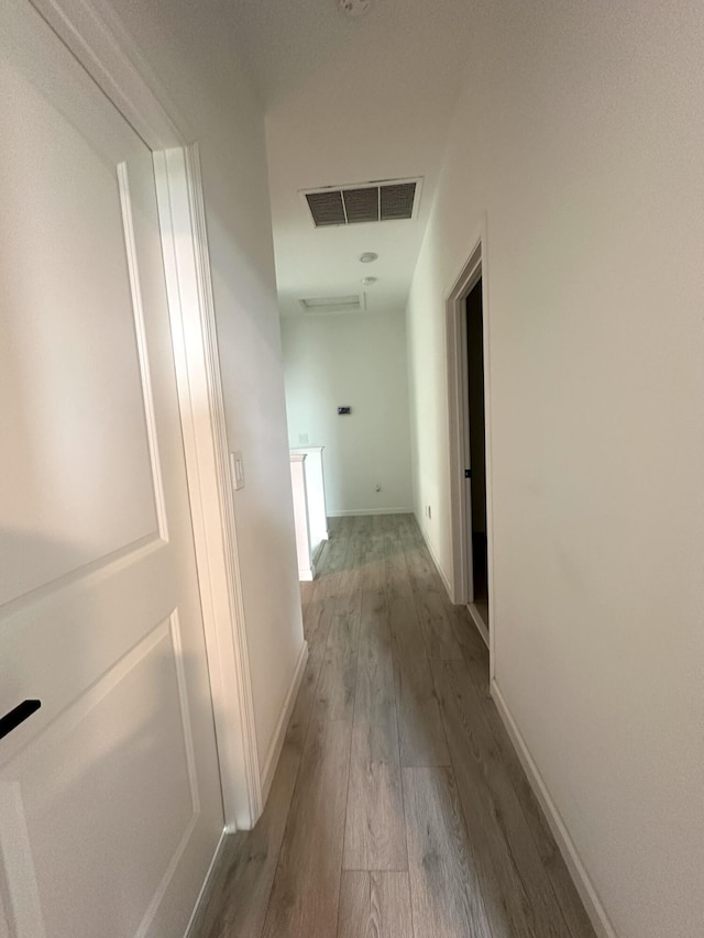 hallway with baseboards, visible vents, and wood finished floors