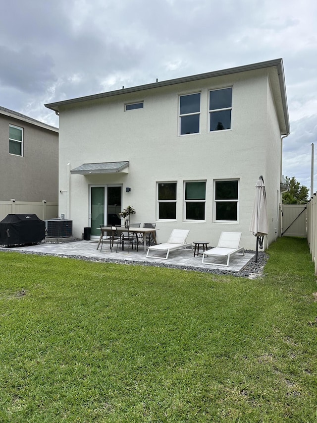 back of house with stucco siding, a lawn, a fenced backyard, a patio area, and a gate