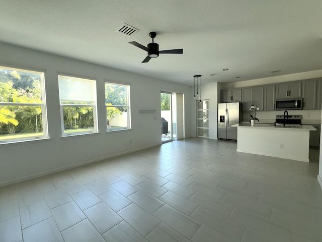 unfurnished living room featuring baseboards, visible vents, ceiling fan, and a sink