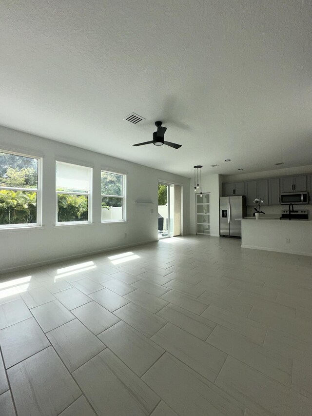 unfurnished living room with a textured ceiling, visible vents, and a ceiling fan