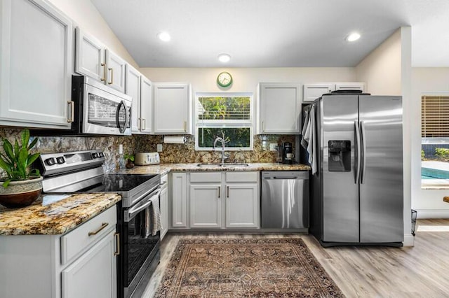 kitchen featuring light wood-style flooring, a sink, backsplash, appliances with stainless steel finishes, and light stone countertops