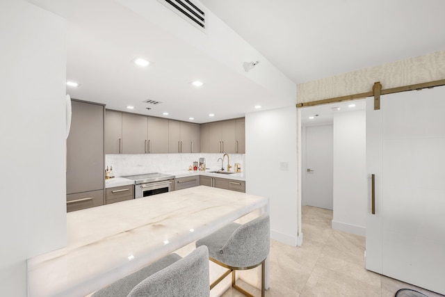 kitchen featuring visible vents, gray cabinetry, a barn door, light countertops, and decorative backsplash