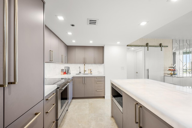 kitchen featuring a barn door, stainless steel electric range, gray cabinetry, and a sink