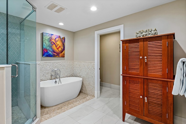 bathroom with visible vents, a freestanding bath, a stall shower, marble finish floor, and tile walls