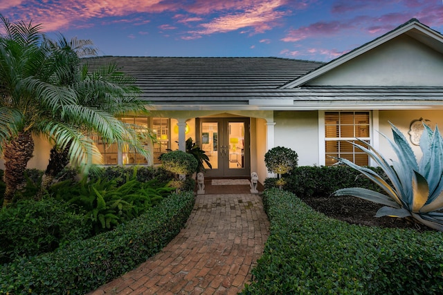 exterior entry at dusk featuring stucco siding and french doors