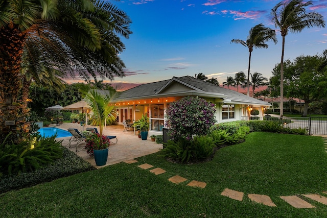 back of house at dusk featuring a fenced in pool, fence, stucco siding, a lawn, and a patio