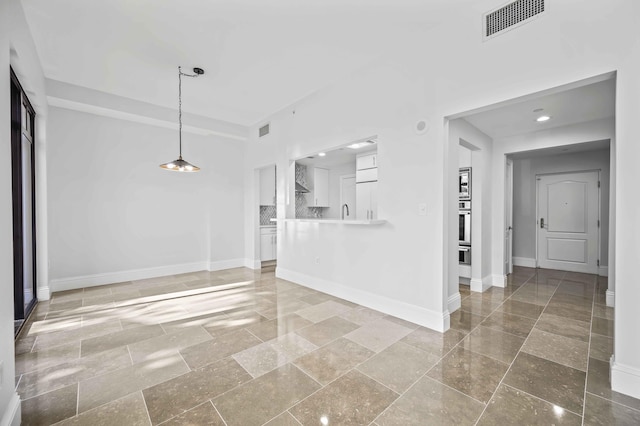 unfurnished living room with stone tile flooring, visible vents, and baseboards