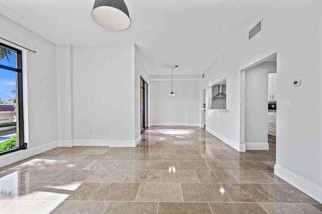 spare room with visible vents, baseboards, plenty of natural light, and stone tile floors