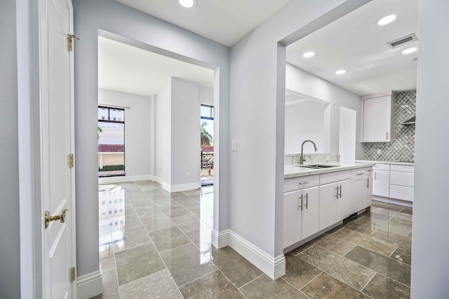 interior space featuring baseboards, a sink, light countertops, white cabinets, and backsplash