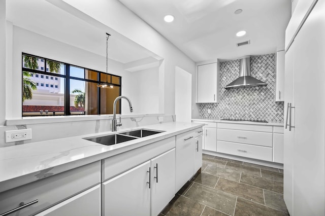 kitchen featuring visible vents, a sink, white cabinets, wall chimney range hood, and backsplash