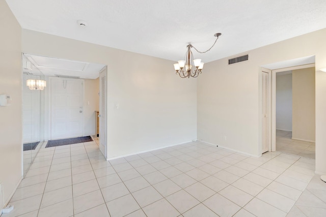 empty room featuring light tile patterned flooring, visible vents, baseboards, and an inviting chandelier