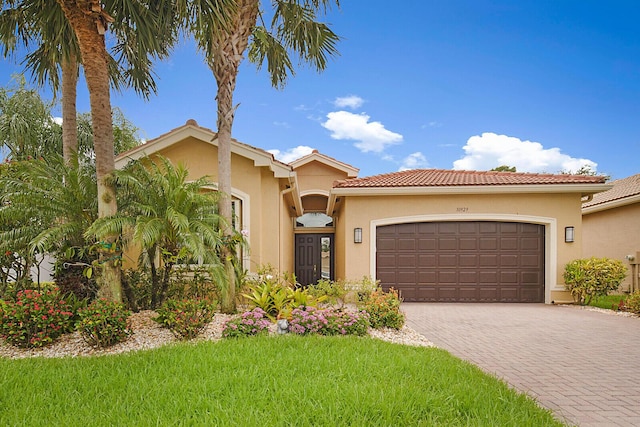 mediterranean / spanish house featuring a tiled roof, a garage, driveway, and stucco siding