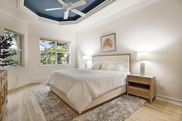 bedroom featuring light wood-style flooring, crown molding, a raised ceiling, and baseboards