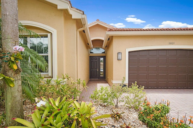 property entrance with stucco siding, a tile roof, decorative driveway, and a garage