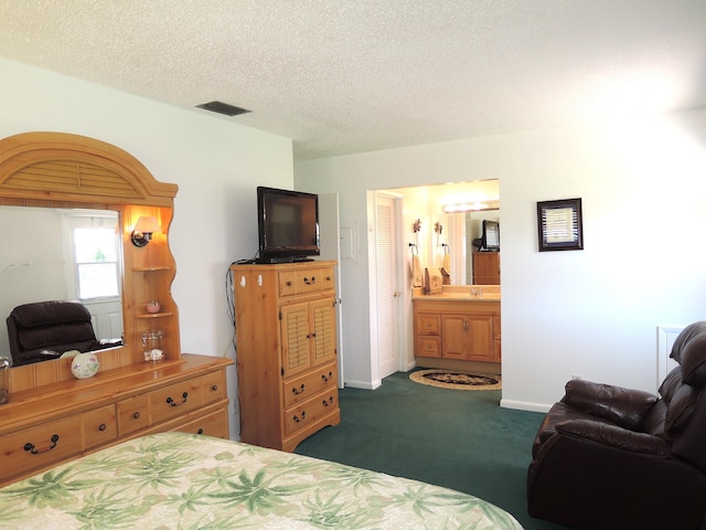 bedroom with visible vents, connected bathroom, baseboards, dark carpet, and a textured ceiling