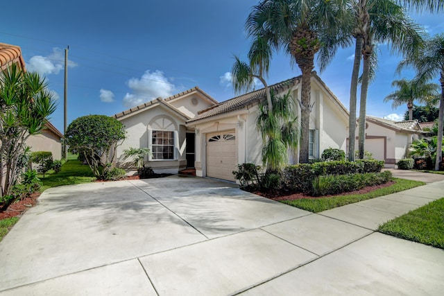 mediterranean / spanish house with a tiled roof, stucco siding, an attached garage, and driveway