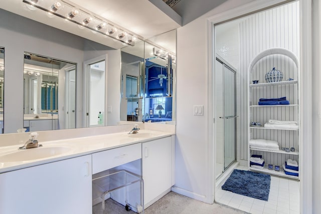 full bath featuring double vanity, baseboards, a stall shower, and a sink