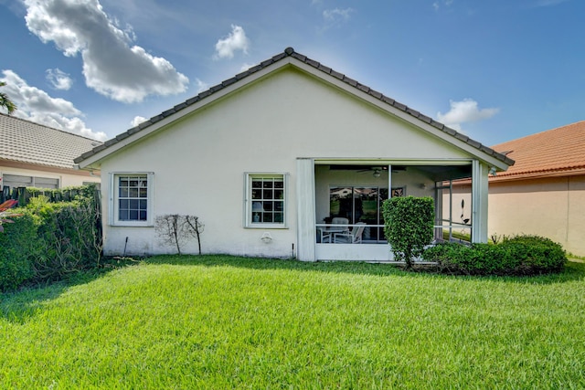 rear view of property featuring stucco siding, a lawn, and a sunroom