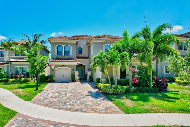 mediterranean / spanish-style house with stucco siding, a tile roof, decorative driveway, an attached garage, and a front yard