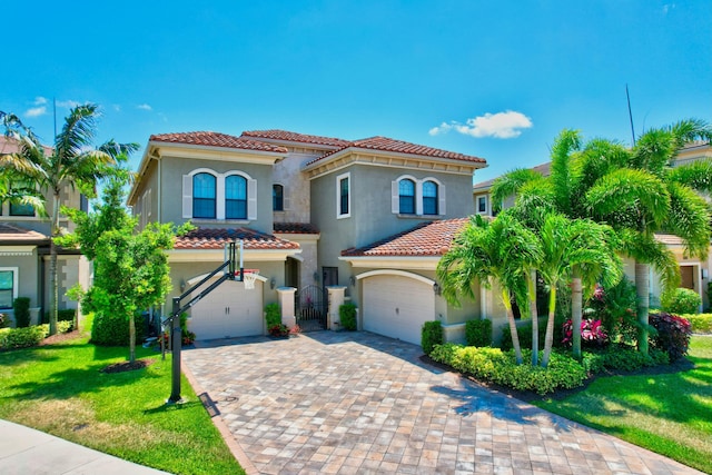 mediterranean / spanish-style house featuring stucco siding, a tile roof, decorative driveway, a front yard, and a garage