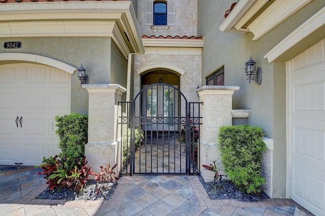 view of exterior entry with stucco siding, a tiled roof, an attached garage, and a gate