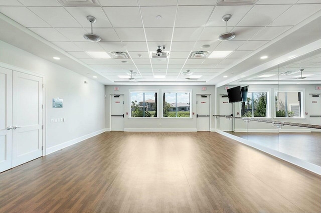 exercise room featuring visible vents, a paneled ceiling, baseboards, and wood finished floors