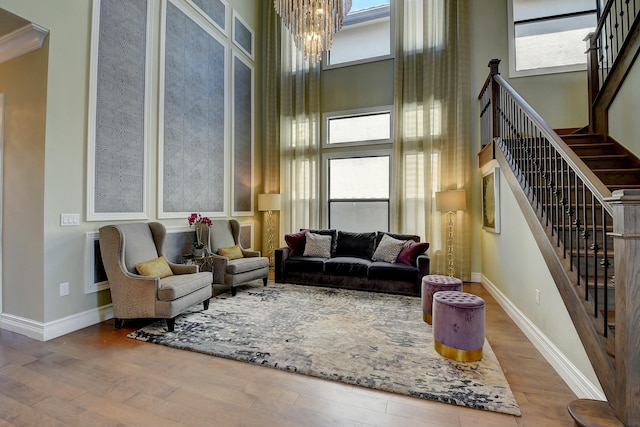 living area featuring baseboards, stairway, wood finished floors, an inviting chandelier, and a towering ceiling