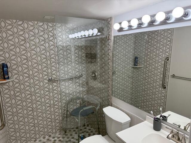 bathroom featuring toilet, tiled shower, and vanity