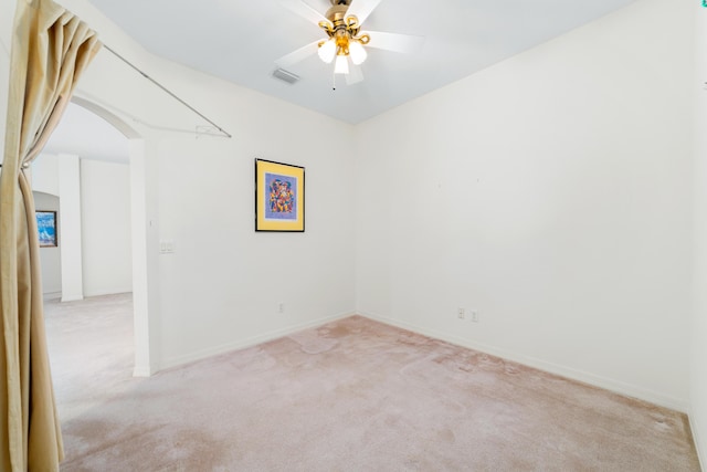 empty room featuring visible vents, baseboards, ceiling fan, light carpet, and arched walkways