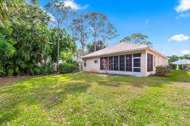 rear view of property with stucco siding, a tile roof, a yard, and a sunroom