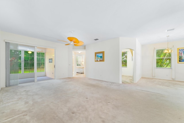 carpeted spare room featuring visible vents, arched walkways, and ceiling fan with notable chandelier