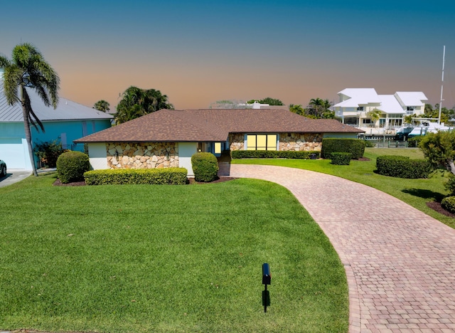 ranch-style home featuring stone siding, a lawn, and decorative driveway