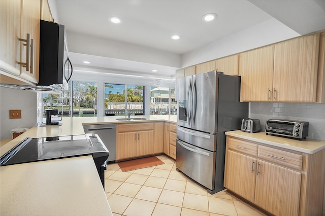 kitchen featuring light brown cabinetry, a sink, stainless steel appliances, a toaster, and light countertops