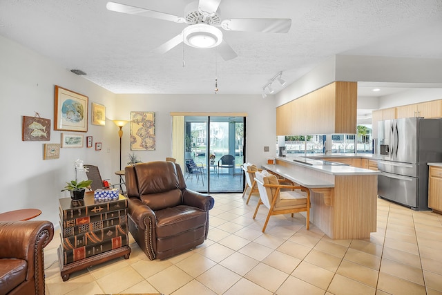 kitchen featuring open floor plan, stainless steel fridge, a peninsula, a breakfast bar area, and light tile patterned floors