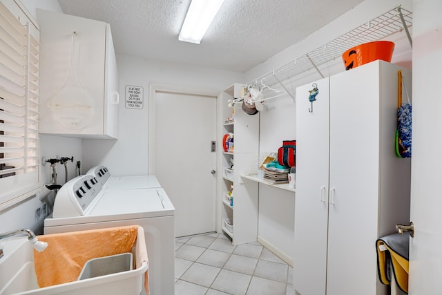 washroom featuring washing machine and clothes dryer, light tile patterned flooring, cabinet space, a sink, and a textured ceiling