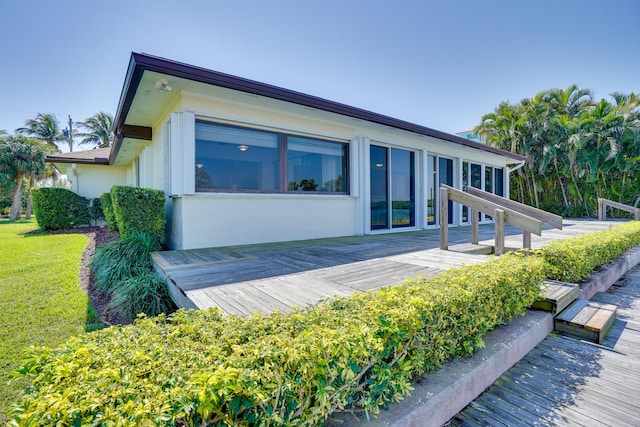 rear view of house with a wooden deck, a lawn, and stucco siding