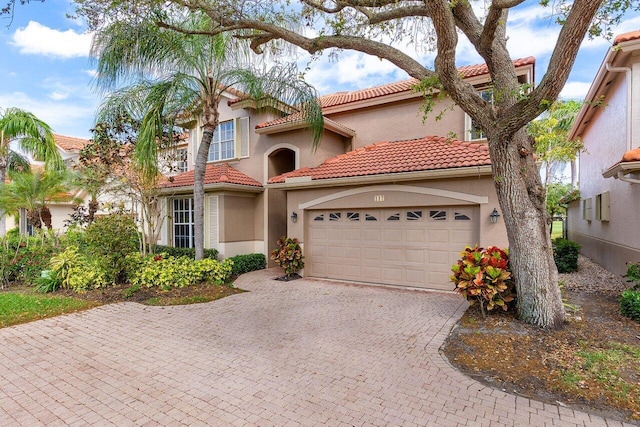 mediterranean / spanish home featuring stucco siding, a tiled roof, decorative driveway, and a garage