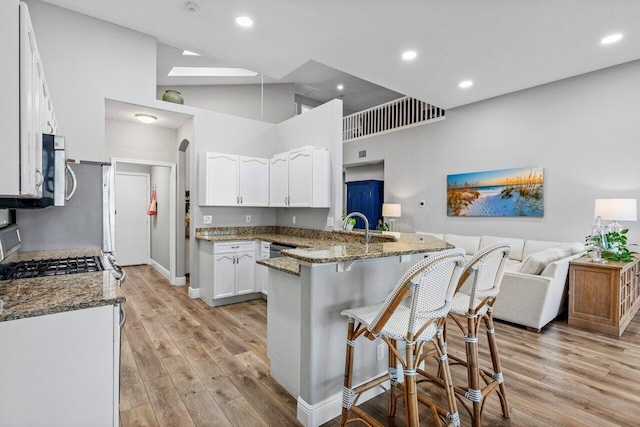 kitchen featuring a breakfast bar, a peninsula, dark stone countertops, and white cabinetry