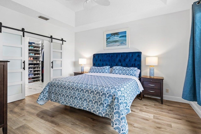 bedroom featuring a barn door, a spacious closet, wood finished floors, and visible vents