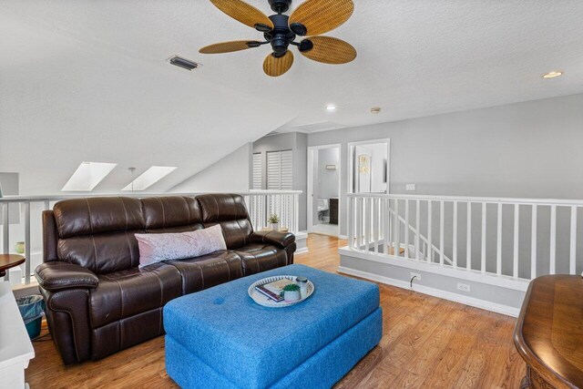 living area featuring visible vents, a textured ceiling, wood finished floors, vaulted ceiling with skylight, and baseboards