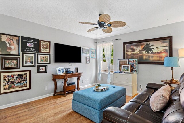 living area with ceiling fan, a textured ceiling, baseboards, and light wood-style floors