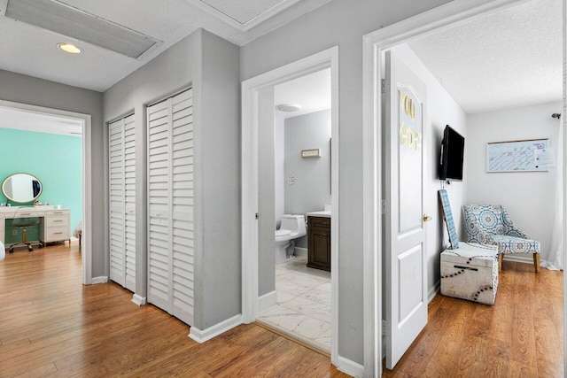 hall featuring baseboards, light wood finished floors, and a textured ceiling