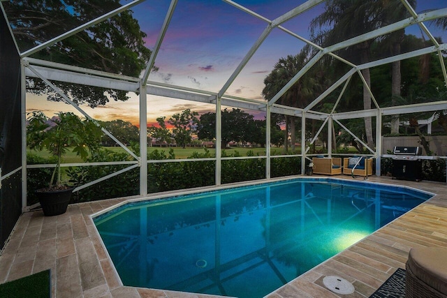 pool at dusk featuring an outdoor pool, a patio, area for grilling, and a lanai