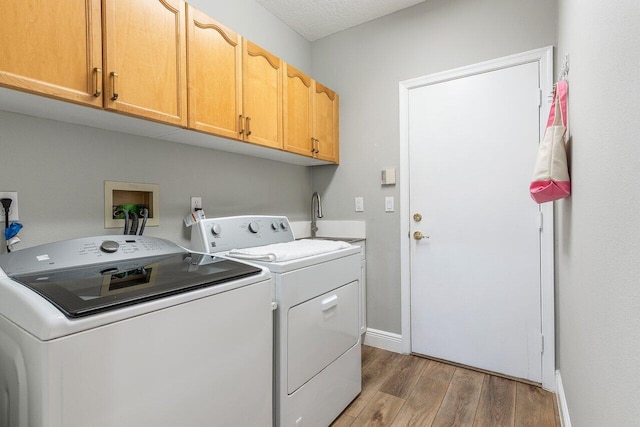 clothes washing area featuring washer and dryer, a sink, cabinet space, light wood finished floors, and baseboards