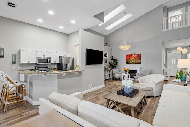 living room featuring light wood-type flooring, visible vents, high vaulted ceiling, and a glass covered fireplace