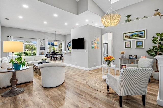 living area with light wood-style floors, visible vents, arched walkways, and a chandelier