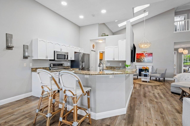 kitchen with a breakfast bar area, wood finished floors, light stone countertops, stainless steel appliances, and white cabinetry