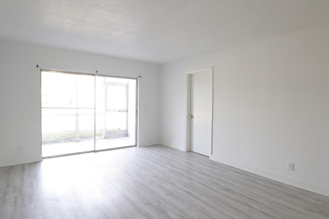 spare room with light wood-style flooring, a textured ceiling, and baseboards