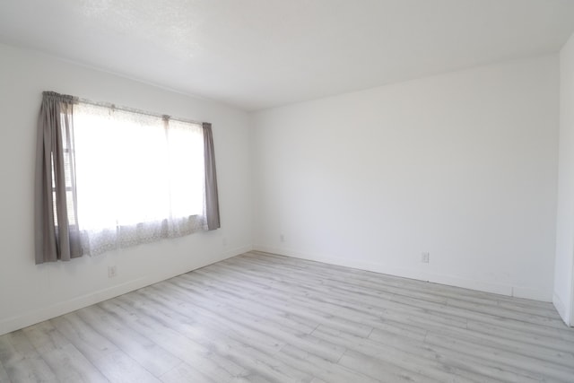 spare room featuring baseboards and light wood finished floors