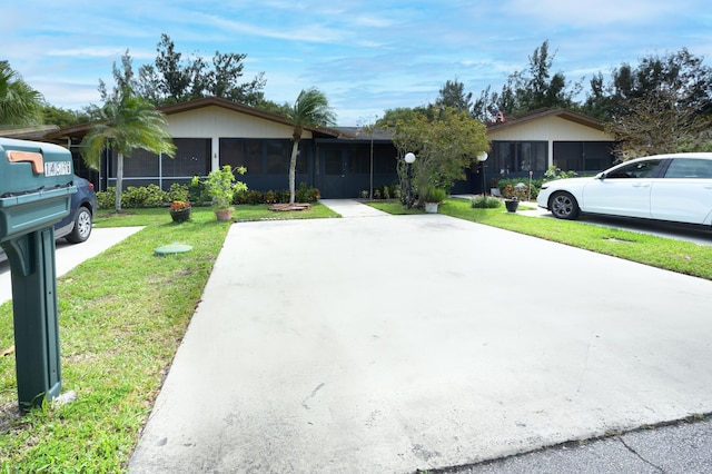ranch-style home featuring concrete driveway, a front yard, and a sunroom